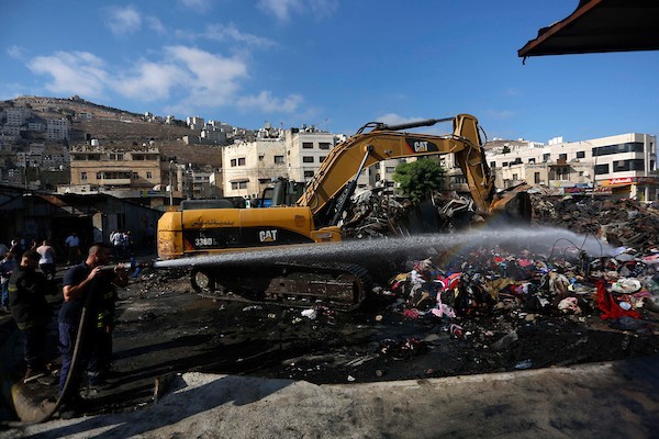 فلسطينيون يتفقدون آثار الحريق الذي التهم محالهم وبسطاتهم في سوق لبيع البضائع المستعملة في المنطقة الشرقية في مدينة نابلس