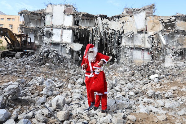   فلسطيني وابنه يرتديان زي بابا نويل يسيران بالقرب من ركام برج الجوهرة الذي تعرض للقصف خلال التصعيد الإسرائيلي الأخير على قطاع غزة.