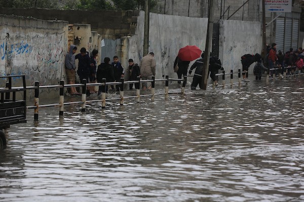 طلاب مدارس الأونروا يسيرون في شارع غمرته المياه وسط الأمطار الغزيرة في مدينة غزة 