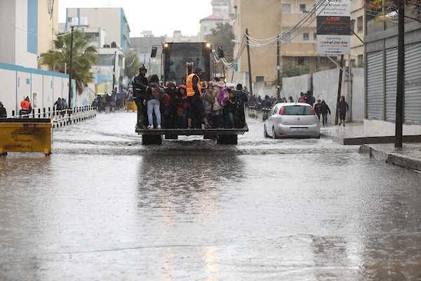 طلاب مدارس الأونروا يسيرون في شارع غمرته المياه وسط الأمطار الغزيرة في مدينة غزة 