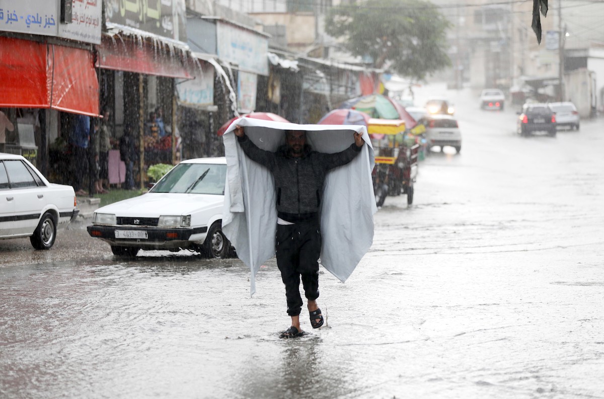 فلسطينيون يسيرون في شارع غمرته مياه الأمطار في دير البلح وسط قطاع غزة 32.jpg