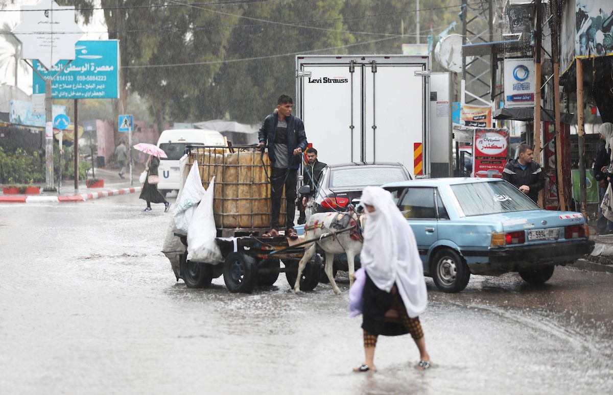 فلسطينيون يسيرون في شارع غمرته مياه الأمطار في دير البلح وسط قطاع غزة 34.jpg