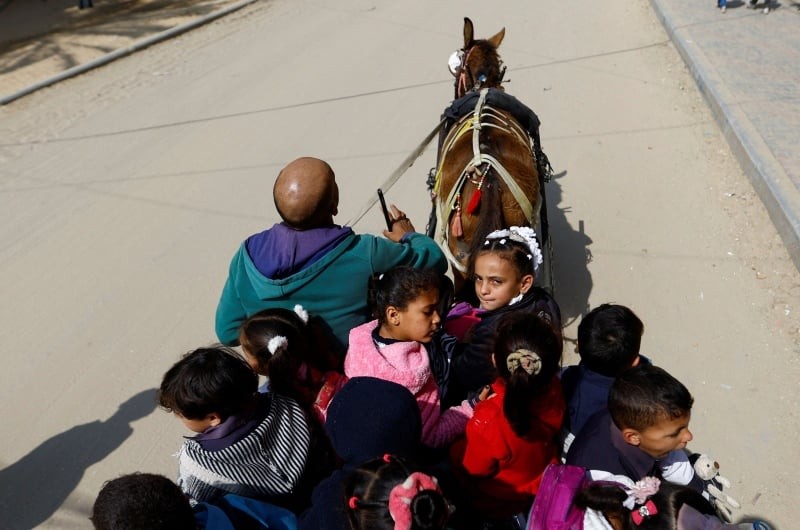 رجل فلسطيني يدعي لؤي أبو سحلول يوفر لبعض الطلاب رحلة بواسطة عربة بحمار إلى المدرسة في خان يونس جنوب قطاع غزة يوم 27 فبراير شباط 2023. تصوير: إبراهيم أبو مصطفى - رويترز.
