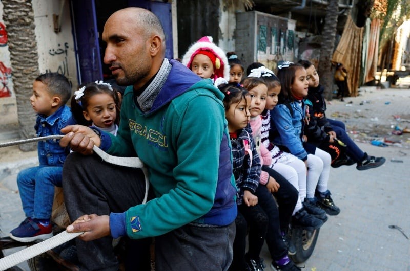 رجل فلسطيني يدعي لؤي أبو سحلول يوفر لبعض الطلاب رحلة بواسطة عربة بحمار إلى المدرسة في خان يونس جنوب قطاع غزة يوم 27 فبراير شباط 2023. تصوير: إبراهيم أبو مصطفى - رويترز.