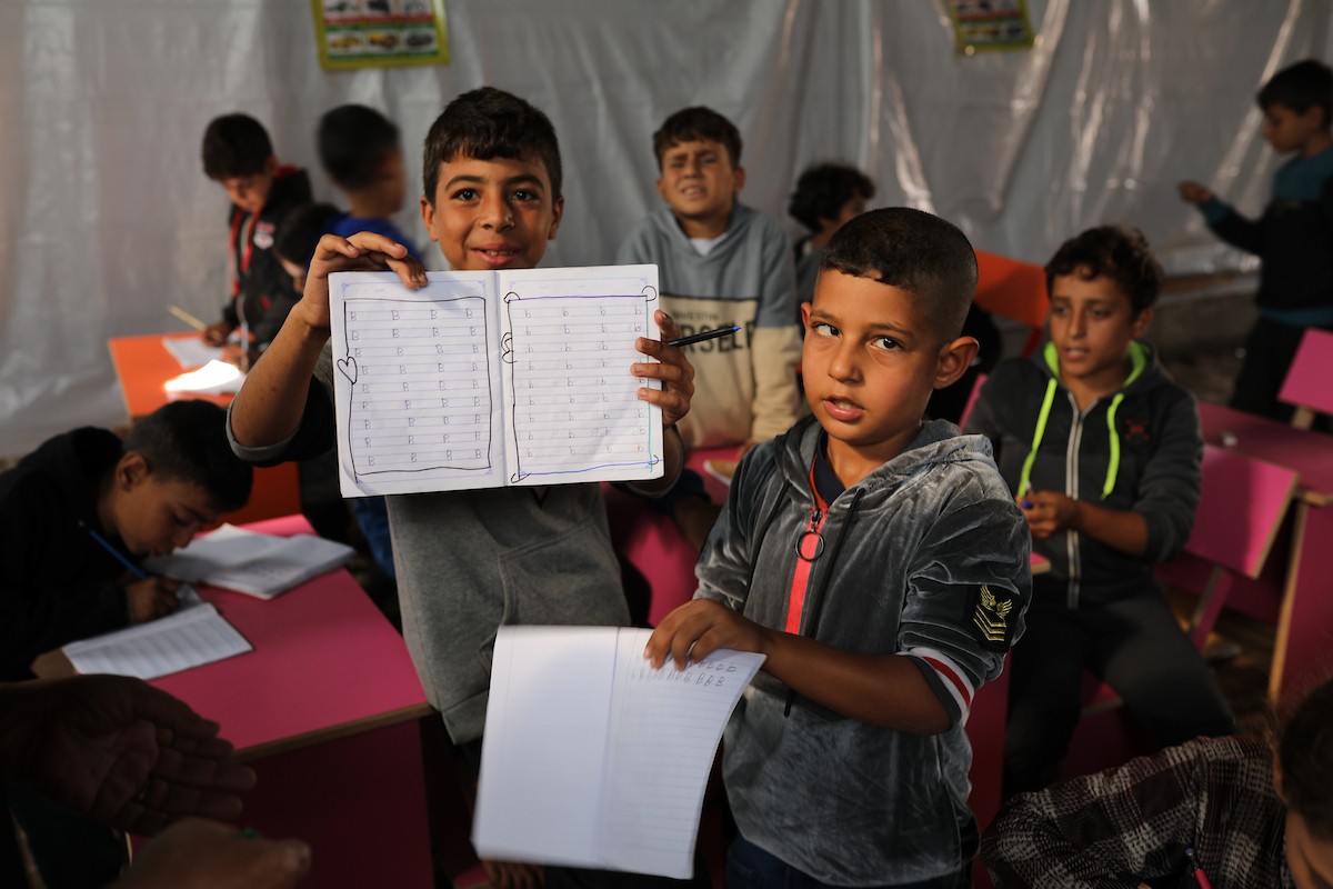 أطفال فلسطينيون نازحون يحضرون درسًا داخل خيمة تُستخدم كفصل دراسي مؤقت في ملجأ بدير البلح.jpg