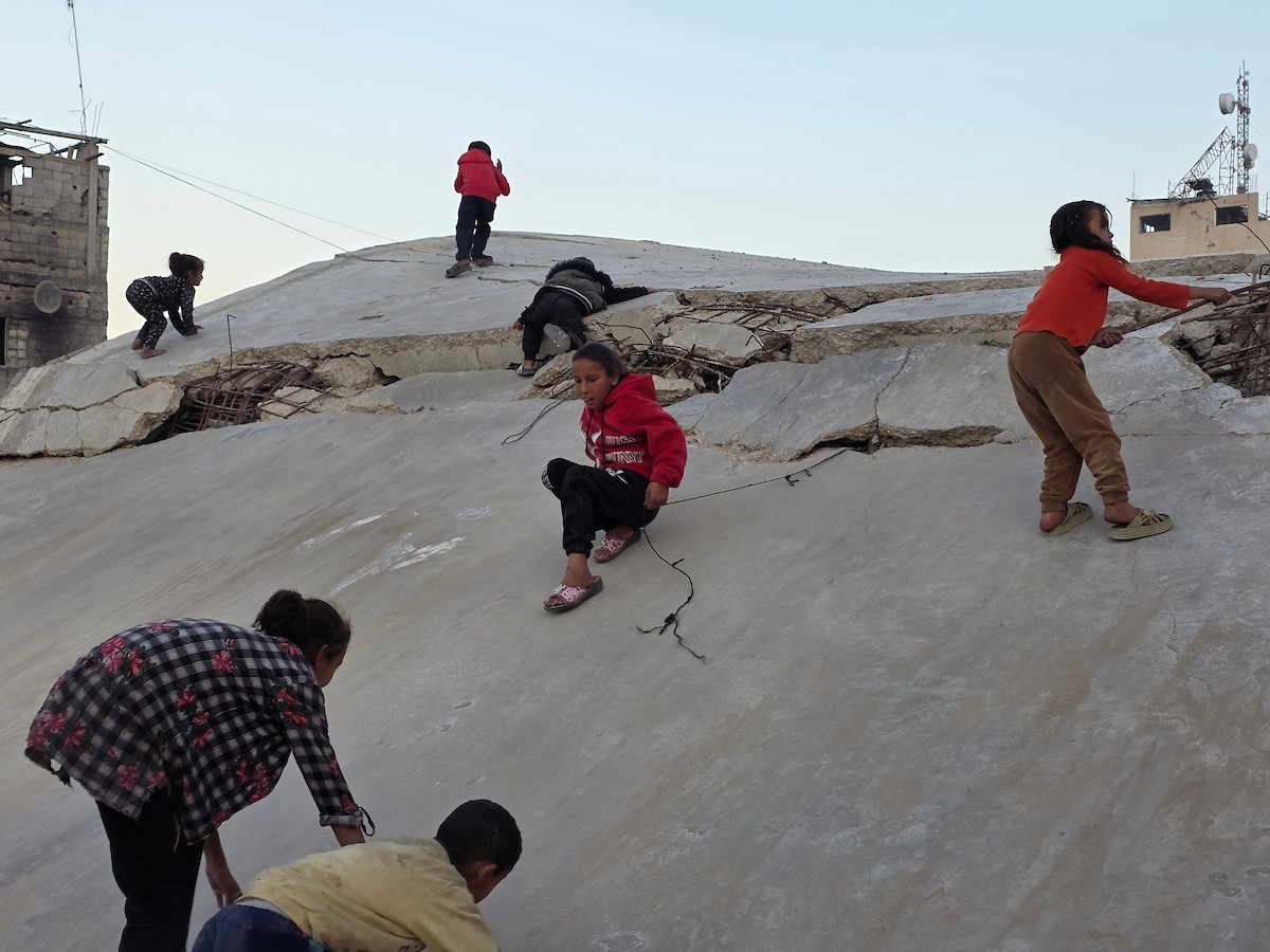 أطفال فلسطينيون يمشون على أسطح منازلهم المدمرة جراء الحرب الإسرائيلية في خان يونس.jpg