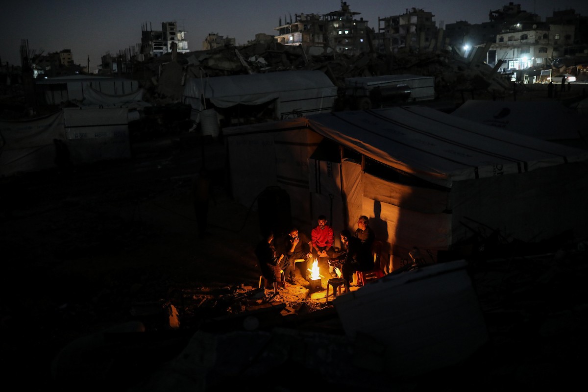 يعيش الفلسطينيون حياتهم اليومية ليلاً في خيام نصبت فوق أنقاض المباني المدمرة في حي الشيخ رضوان وسط مدينة غزة، 5 ديسمبر/كانون الأول 2025.تصوير: عمر أشتوي