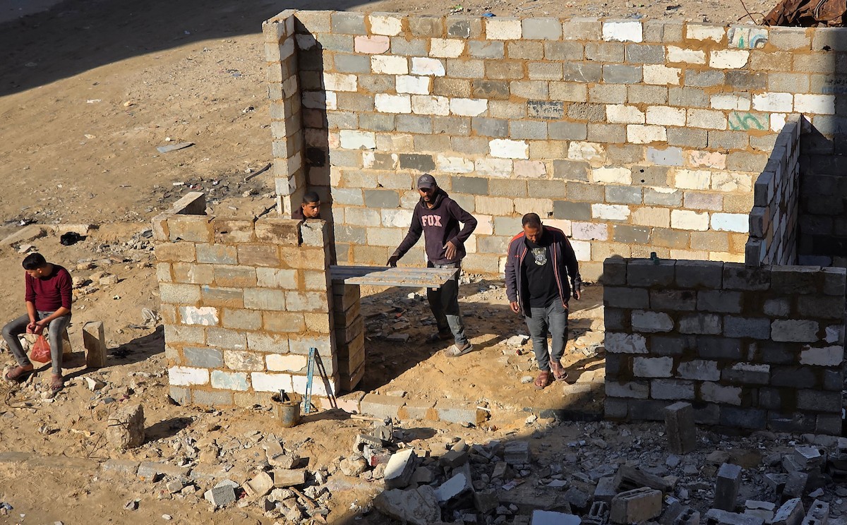 في خان يونس، جنوب قطاع غزة، يقوم أصحاب المتاجر الفلسطينيون بإزالة الأنقاض بأيديهم، ويعيدون بناء متاجرهم المتضررة باستخدام الحجارة والطين الأحمر، 27 ديسمبر/كانون الأول 2025 (صورة: طارق محمد)