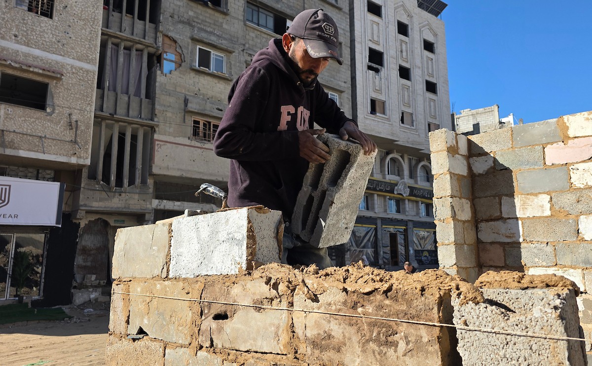 في خان يونس، جنوب قطاع غزة، يقوم أصحاب المتاجر الفلسطينيون بإزالة الأنقاض بأيديهم، ويعيدون بناء متاجرهم المتضررة باستخدام الحجارة والطين الأحمر، 27 ديسمبر/كانون الأول 2025 (صورة: طارق محمد)