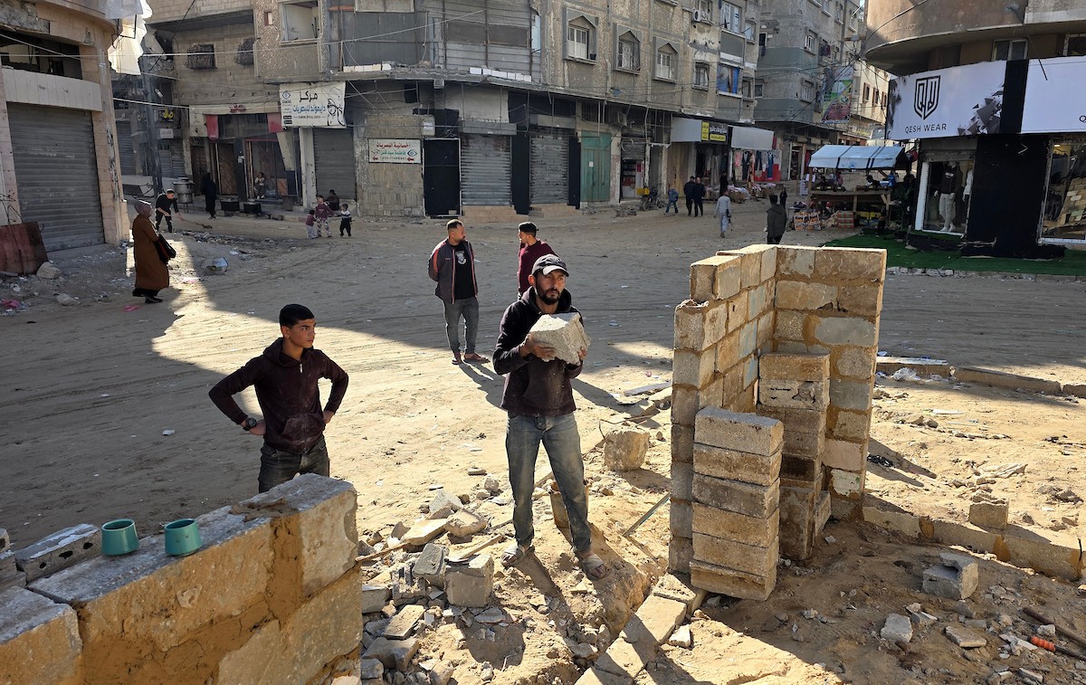 في خان يونس، جنوب قطاع غزة، يقوم أصحاب المتاجر الفلسطينيون بإزالة الأنقاض بأيديهم، ويعيدون بناء متاجرهم المتضررة باستخدام الحجارة والطين الأحمر، 27 ديسمبر/كانون الأول 2025 (صورة: طارق محمد)