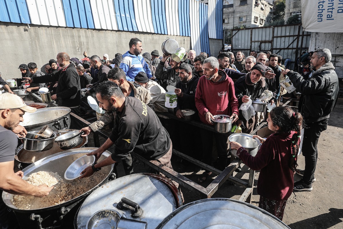 يتلقى فلسطينيون في مخيم النصيرات وسط قطاع غزة وجبات ساخنة من جمعية خيرية تُعنى بالنازحين جراء الهجمات الإسرائيلية، بينما يتجمع حشد كبير، يضم نساءً وأطفالاً، خلال عملية التوزيع، في 30 ديسمبر/كانون الأول 2025. صورة: معز صالحي