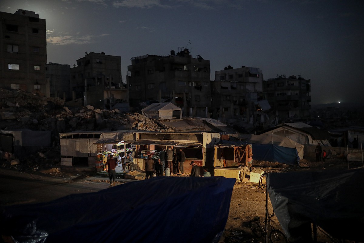 يعيش الفلسطينيون حياتهم اليومية ليلاً في خيام نصبت فوق أنقاض المباني المدمرة في حي الشيخ رضوان وسط مدينة غزة، 5 ديسمبر/كانون الأول 2025.تصوير: عمر أشتوي