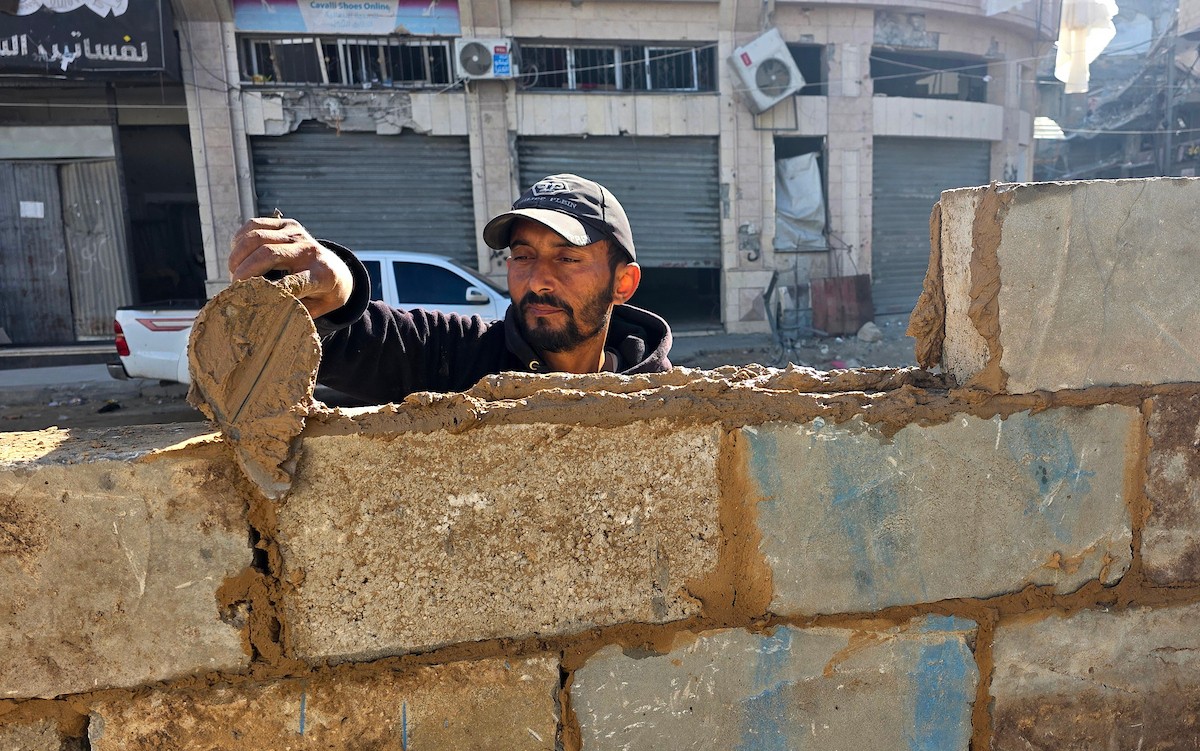 في خان يونس، جنوب قطاع غزة، يقوم أصحاب المتاجر الفلسطينيون بإزالة الأنقاض بأيديهم، ويعيدون بناء متاجرهم المتضررة باستخدام الحجارة والطين الأحمر، 27 ديسمبر/كانون الأول 2025 (صورة: طارق محمد)