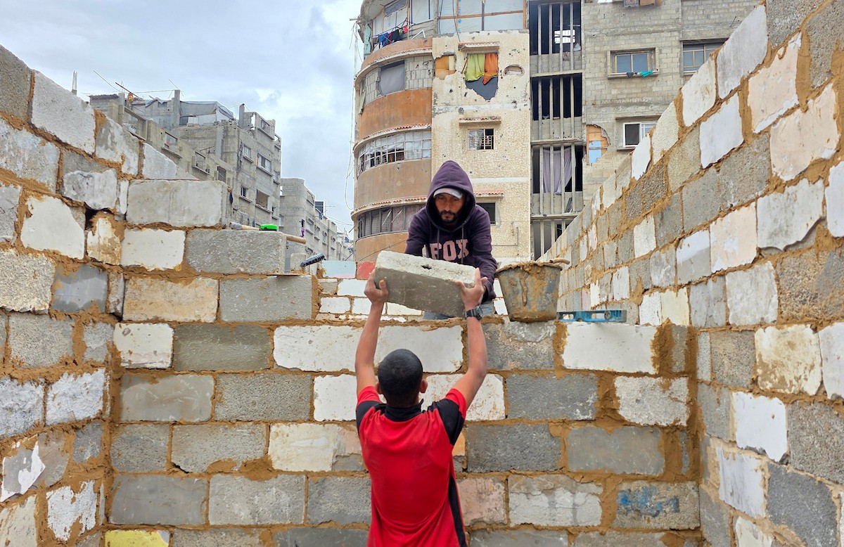 في خان يونس، جنوب قطاع غزة، يقوم أصحاب المتاجر الفلسطينيون بإزالة الأنقاض بأيديهم، ويعيدون بناء متاجرهم المتضررة باستخدام الحجارة والطين الأحمر، 27 ديسمبر/كانون الأول 2025 (صورة: طارق محمد)