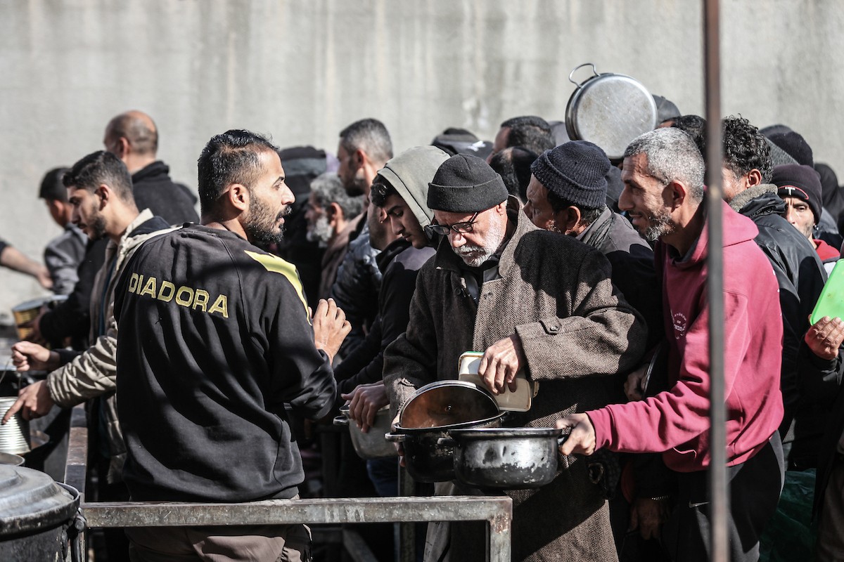 يتلقى فلسطينيون في مخيم النصيرات وسط قطاع غزة وجبات ساخنة من جمعية خيرية تُعنى بالنازحين جراء الهجمات الإسرائيلية، بينما يتجمع حشد كبير، يضم نساءً وأطفالاً، خلال عملية التوزيع، في 30 ديسمبر/كانون الأول 2025. صورة: معز صالحي