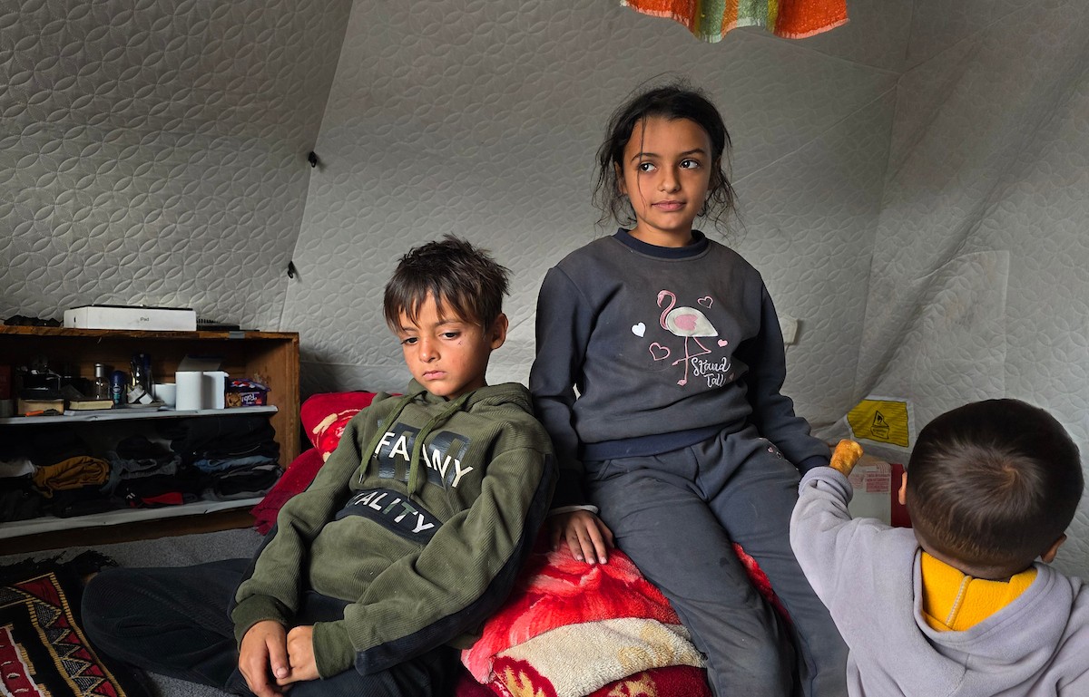 عائلة فلسطينية تحتمي من برد الشتاء القارس في خيمة نصبتها فوق منزلها المدمر قرب الخط الأصفر في خان يونس، جنوب قطاع غزة، ١٧ ديسمبر/كانون الأول ٢٠٢٥. تصوير: طارق محمد/وكالة الأنباء الفلسطينية (APA )