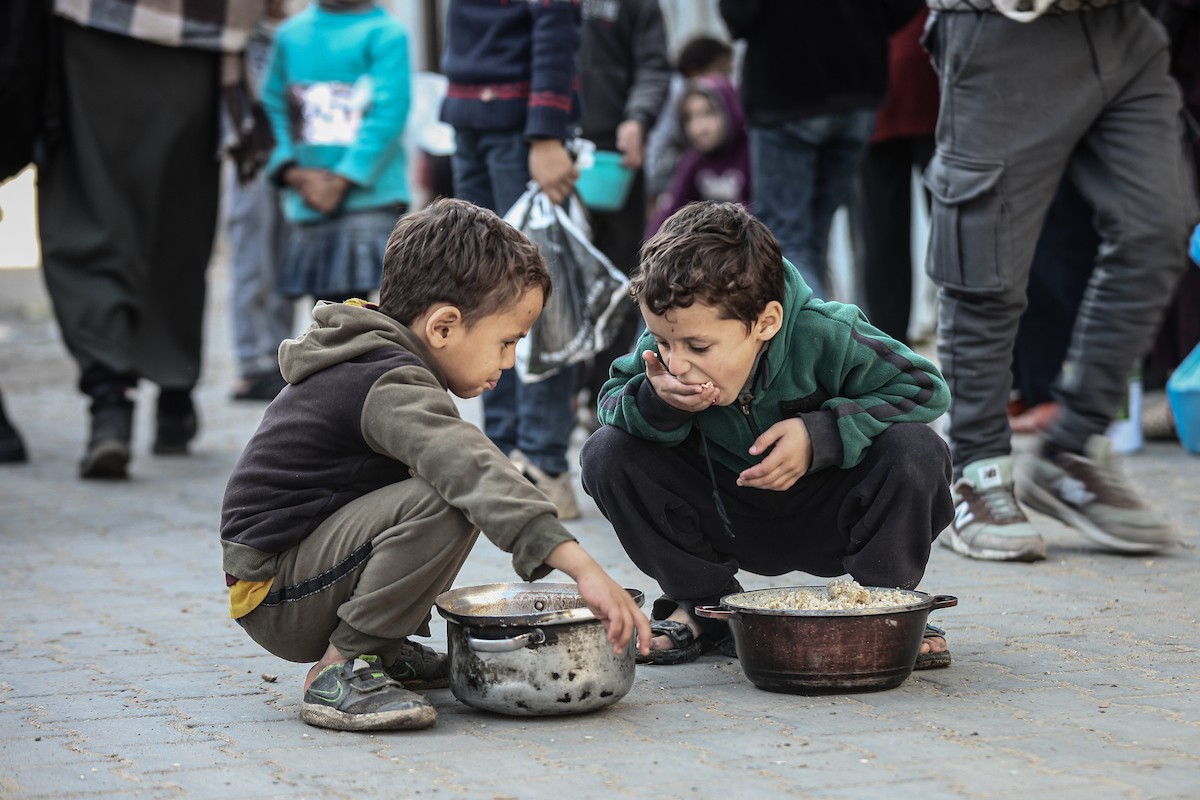 يتلقى فلسطينيون في مخيم النصيرات وسط قطاع غزة وجبات ساخنة من جمعية خيرية تُعنى بالنازحين جراء الهجمات الإسرائيلية، بينما يتجمع حشد كبير، يضم نساءً وأطفالاً، خلال عملية التوزيع، في 30 ديسمبر/كانون الأول 2025. صورة: معز صالحي