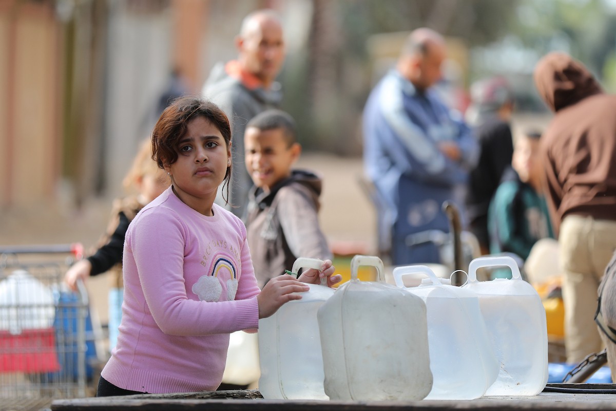 يتجمع الفلسطينيون لتلقي مياه الشرب مجانًا في مخيم البريج للاجئين، في ظل تفاقم أزمة نقص المياه وتدهور البنية التحتية، 21 ديسمبر/كانون الأول 2025. صورة: رمزي أبو عامر