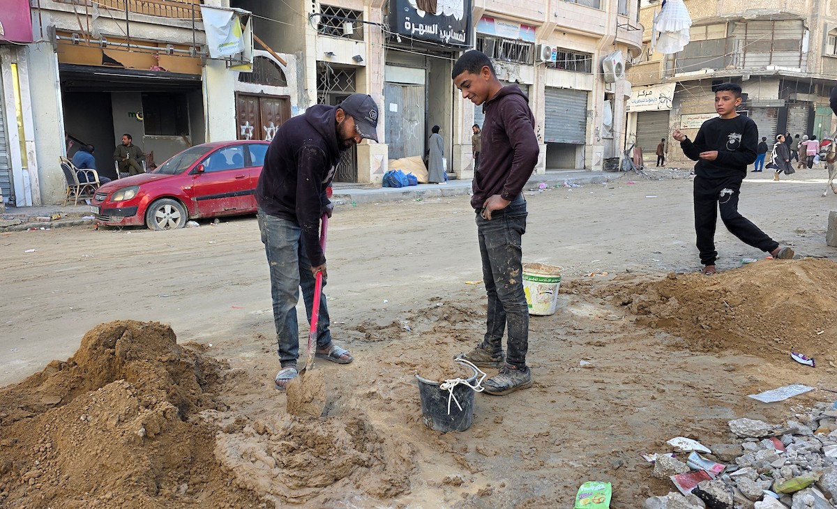 في خان يونس، جنوب قطاع غزة، يقوم أصحاب المتاجر الفلسطينيون بإزالة الأنقاض بأيديهم، ويعيدون بناء متاجرهم المتضررة باستخدام الحجارة والطين الأحمر، 27 ديسمبر/كانون الأول 2025 (صورة: طارق محمد)