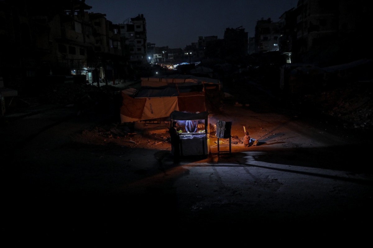يعيش الفلسطينيون حياتهم اليومية ليلاً في خيام نصبت فوق أنقاض المباني المدمرة في حي الشيخ رضوان وسط مدينة غزة، 5 ديسمبر/كانون الأول 2025.تصوير: عمر أشتوي