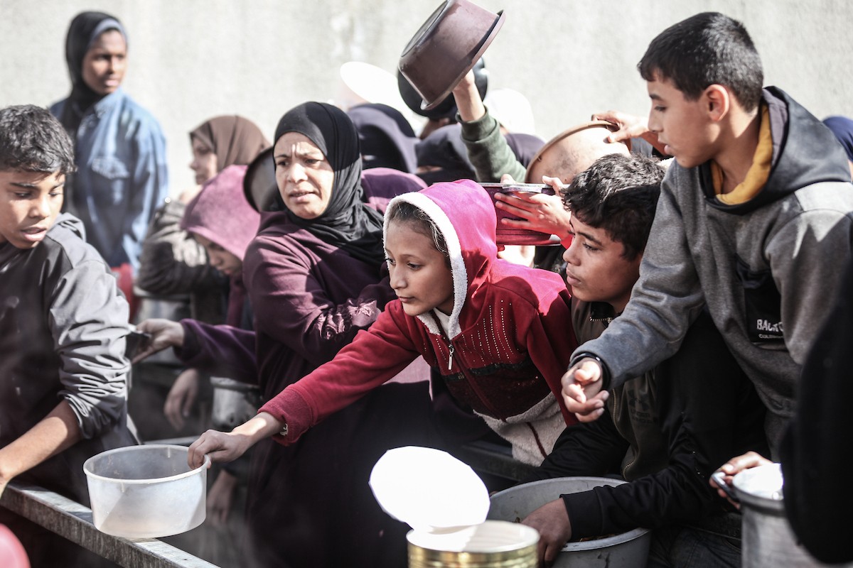 يتلقى فلسطينيون في مخيم النصيرات وسط قطاع غزة وجبات ساخنة من جمعية خيرية تُعنى بالنازحين جراء الهجمات الإسرائيلية، بينما يتجمع حشد كبير، يضم نساءً وأطفالاً، خلال عملية التوزيع، في 30 ديسمبر/كانون الأول 2025. صورة: معز صالحي