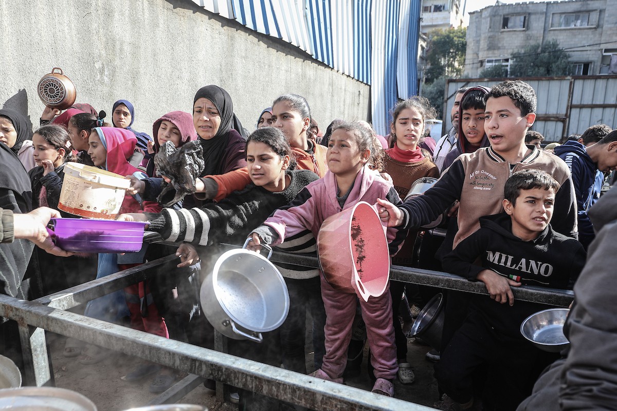 يتلقى فلسطينيون في مخيم النصيرات وسط قطاع غزة وجبات ساخنة من جمعية خيرية تُعنى بالنازحين جراء الهجمات الإسرائيلية، بينما يتجمع حشد كبير، يضم نساءً وأطفالاً، خلال عملية التوزيع، في 30 ديسمبر/كانون الأول 2025. صورة: معز صالحي