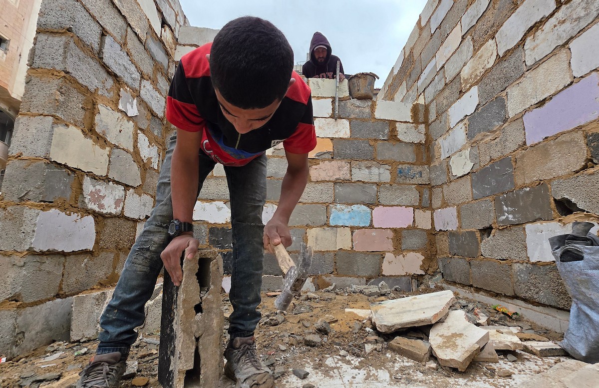 في خان يونس، جنوب قطاع غزة، يقوم أصحاب المتاجر الفلسطينيون بإزالة الأنقاض بأيديهم، ويعيدون بناء متاجرهم المتضررة باستخدام الحجارة والطين الأحمر، 27 ديسمبر/كانون الأول 2025 (صورة: طارق محمد)