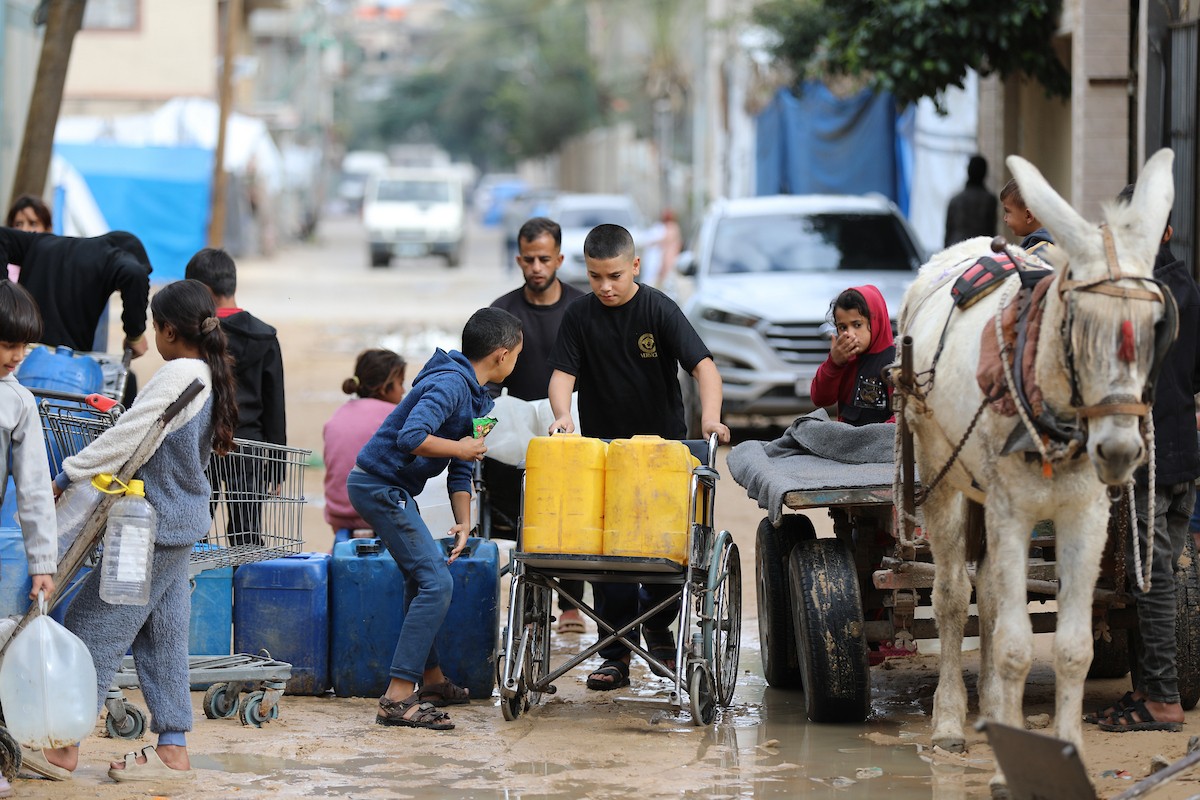 يتجمع الفلسطينيون لتلقي مياه الشرب مجانًا في مخيم البريج للاجئين، في ظل تفاقم أزمة نقص المياه وتدهور البنية التحتية، 21 ديسمبر/كانون الأول 2025. صورة: رمزي أبو عامر