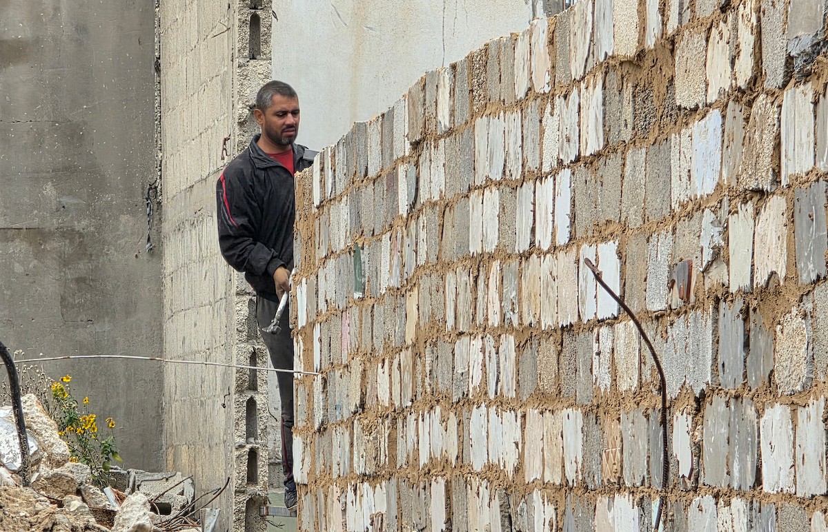 في خان يونس، جنوب قطاع غزة، يقوم أصحاب المتاجر الفلسطينيون بإزالة الأنقاض بأيديهم، ويعيدون بناء متاجرهم المتضررة باستخدام الحجارة والطين الأحمر، 27 ديسمبر/كانون الأول 2025 (صورة: طارق محمد)