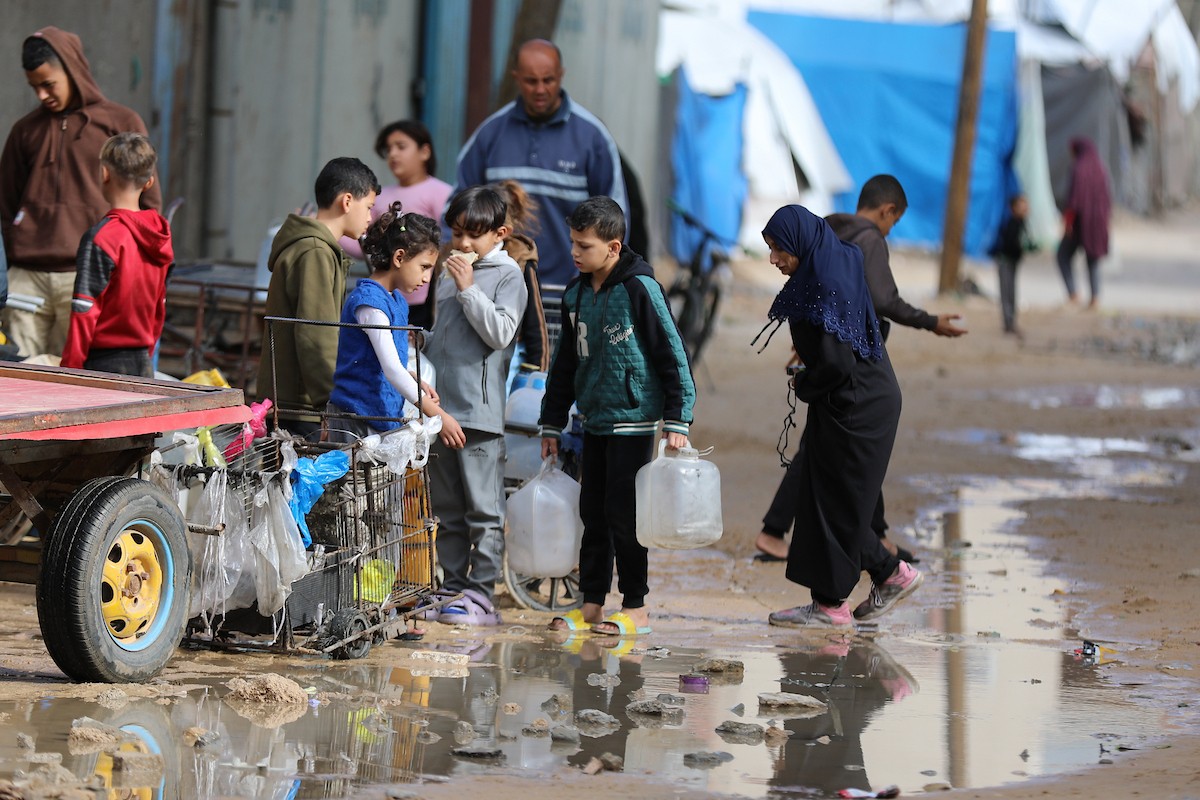 يتجمع الفلسطينيون لتلقي مياه الشرب مجانًا في مخيم البريج للاجئين، في ظل تفاقم أزمة نقص المياه وتدهور البنية التحتية، 21 ديسمبر/كانون الأول 2025. صورة: رمزي أبو عامر