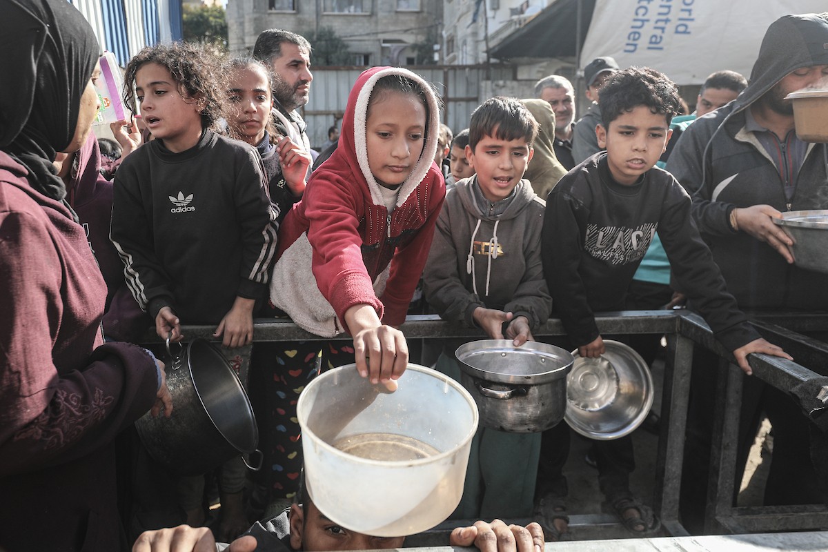 يتلقى فلسطينيون في مخيم النصيرات وسط قطاع غزة وجبات ساخنة من جمعية خيرية تُعنى بالنازحين جراء الهجمات الإسرائيلية، بينما يتجمع حشد كبير، يضم نساءً وأطفالاً، خلال عملية التوزيع، في 30 ديسمبر/كانون الأول 2025. صورة: معز صالحي