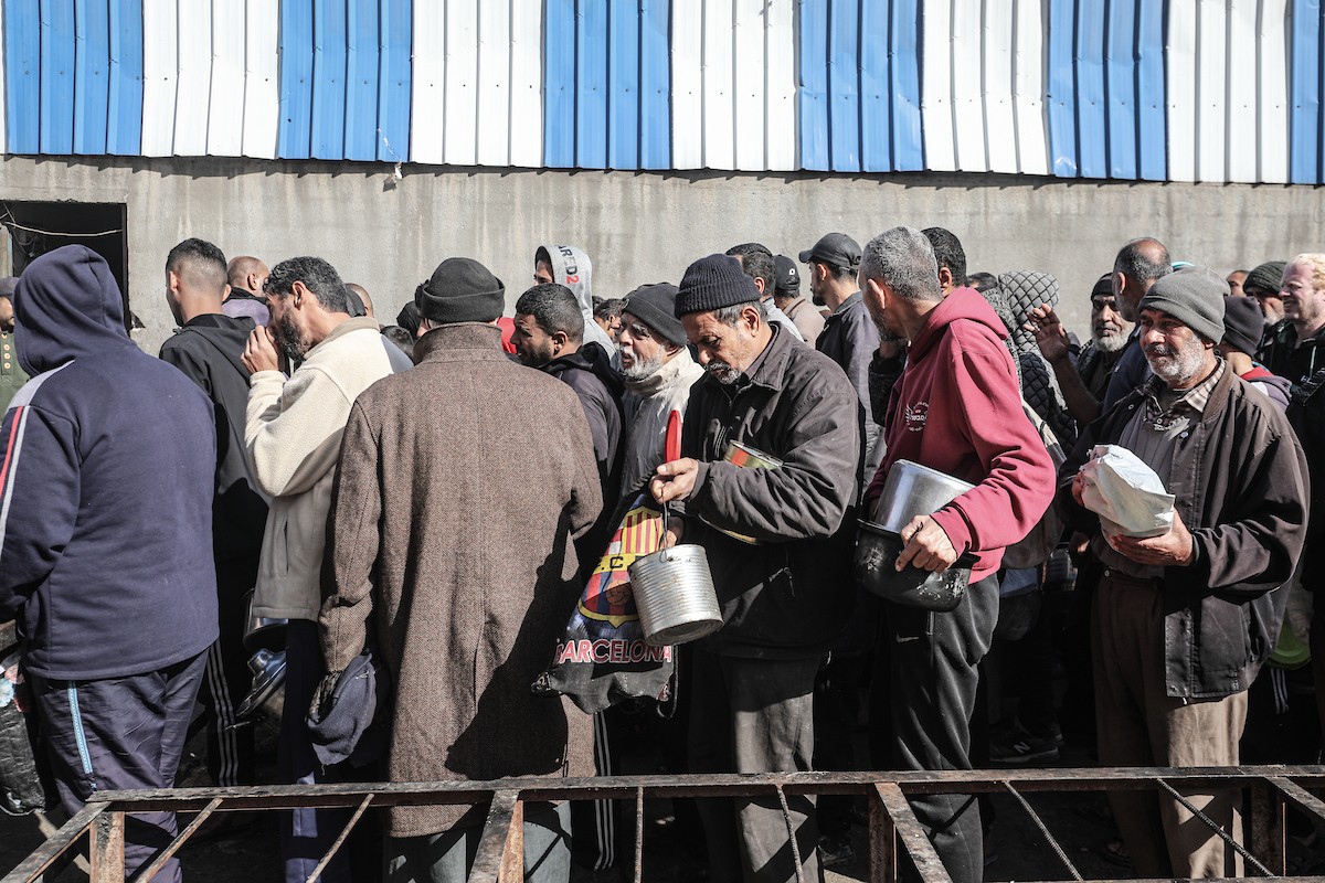 يتلقى فلسطينيون في مخيم النصيرات وسط قطاع غزة وجبات ساخنة من جمعية خيرية تُعنى بالنازحين جراء الهجمات الإسرائيلية، بينما يتجمع حشد كبير، يضم نساءً وأطفالاً، خلال عملية التوزيع، في 30 ديسمبر/كانون الأول 2025. صورة: معز صالحي