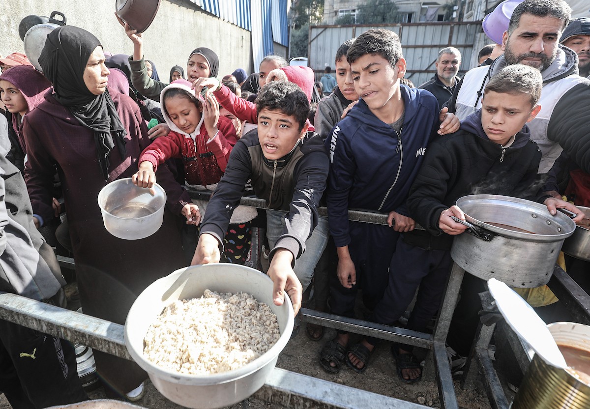 يتلقى فلسطينيون في مخيم النصيرات وسط قطاع غزة وجبات ساخنة من جمعية خيرية تُعنى بالنازحين جراء الهجمات الإسرائيلية، بينما يتجمع حشد كبير، يضم نساءً وأطفالاً، خلال عملية التوزيع، في 30 ديسمبر/كانون الأول 2025. صورة: معز صالحي
