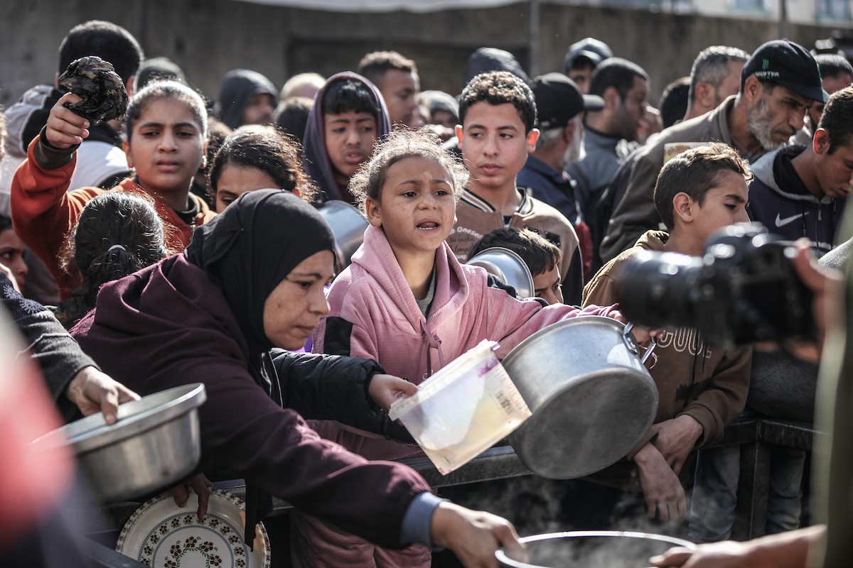 يتلقى فلسطينيون في مخيم النصيرات وسط قطاع غزة وجبات ساخنة من جمعية خيرية تُعنى بالنازحين جراء الهجمات الإسرائيلية، بينما يتجمع حشد كبير، يضم نساءً وأطفالاً، خلال عملية التوزيع، في 30 ديسمبر/كانون الأول 2025. صورة: معز صالحي