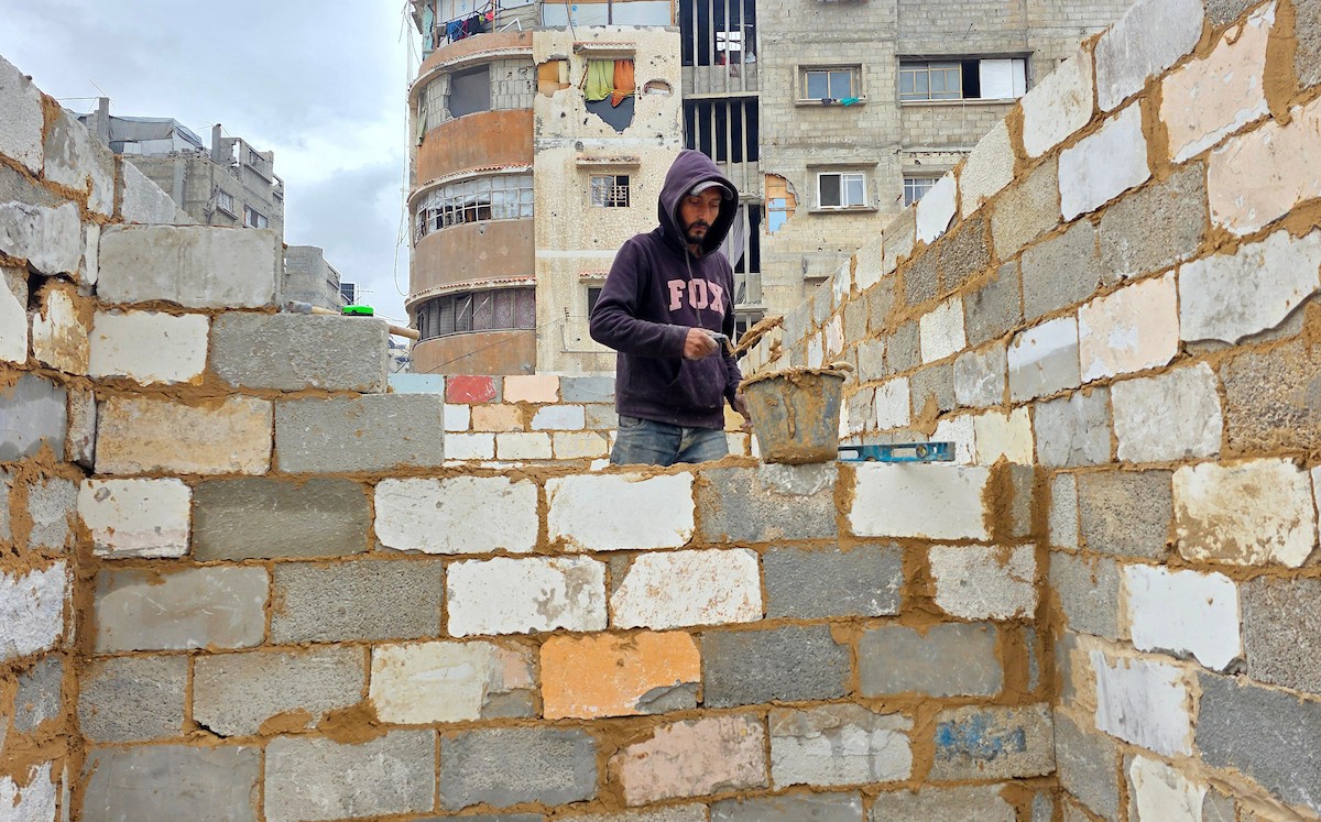 في خان يونس، جنوب قطاع غزة، يقوم أصحاب المتاجر الفلسطينيون بإزالة الأنقاض بأيديهم، ويعيدون بناء متاجرهم المتضررة باستخدام الحجارة والطين الأحمر، 27 ديسمبر/كانون الأول 2025 (صورة: طارق محمد)