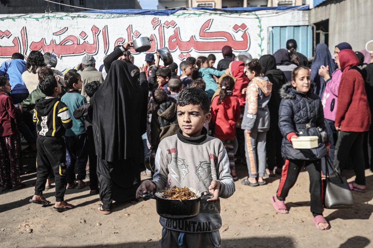 يتلقى فلسطينيون في مخيم النصيرات وسط قطاع غزة وجبات ساخنة من جمعية خيرية تُعنى بالنازحين جراء الهجمات الإسرائيلية، بينما يتجمع حشد كبير، يضم نساءً وأطفالاً، خلال عملية التوزيع، في 30 ديسمبر/كانون الأول 2025. صورة: معز صالحي