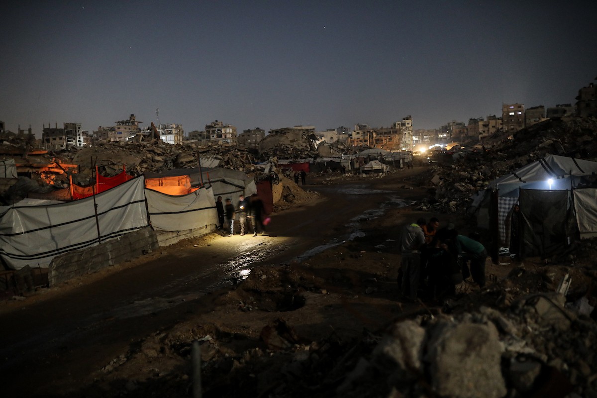 يعيش الفلسطينيون حياتهم اليومية ليلاً في خيام نصبت فوق أنقاض المباني المدمرة في حي الشيخ رضوان وسط مدينة غزة، 5 ديسمبر/كانون الأول 2025.تصوير: عمر أشتوي