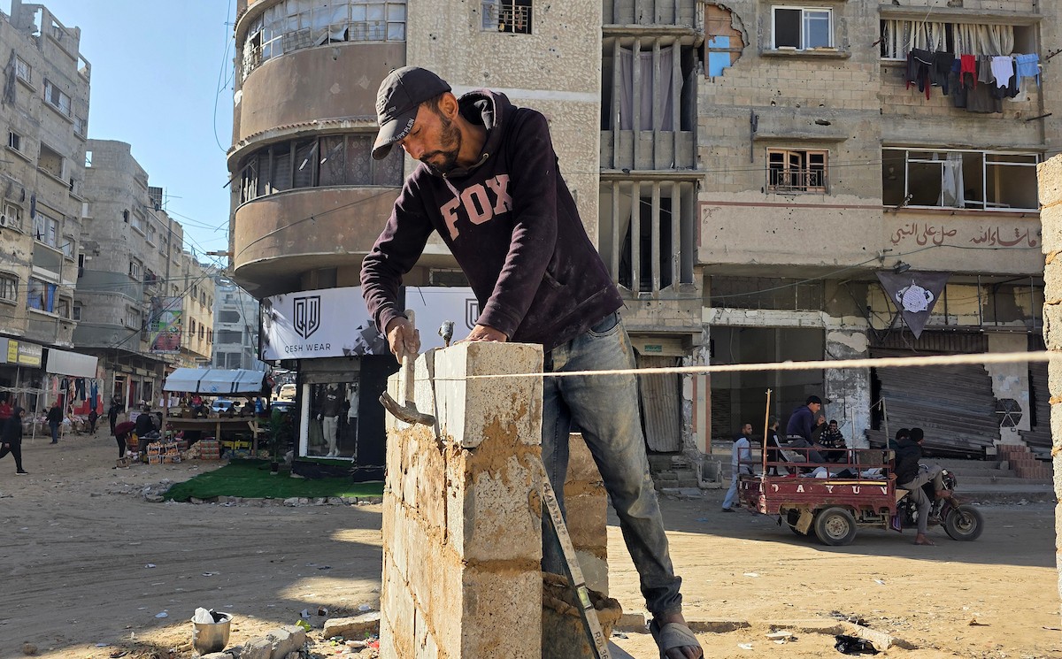 في خان يونس، جنوب قطاع غزة، يقوم أصحاب المتاجر الفلسطينيون بإزالة الأنقاض بأيديهم، ويعيدون بناء متاجرهم المتضررة باستخدام الحجارة والطين الأحمر، 27 ديسمبر/كانون الأول 2025 (صورة: طارق محمد)