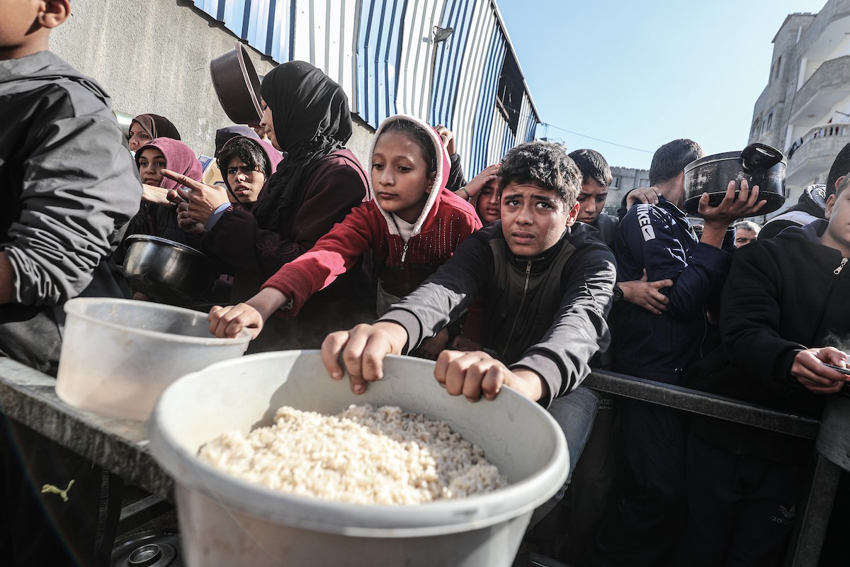 يتلقى فلسطينيون في مخيم النصيرات وسط قطاع غزة وجبات ساخنة من جمعية خيرية تُعنى بالنازحين جراء الهجمات الإسرائيلية، بينما يتجمع حشد كبير، يضم نساءً وأطفالاً، خلال عملية التوزيع، في 30 ديسمبر/كانون الأول 2025. صورة: معز صالحي