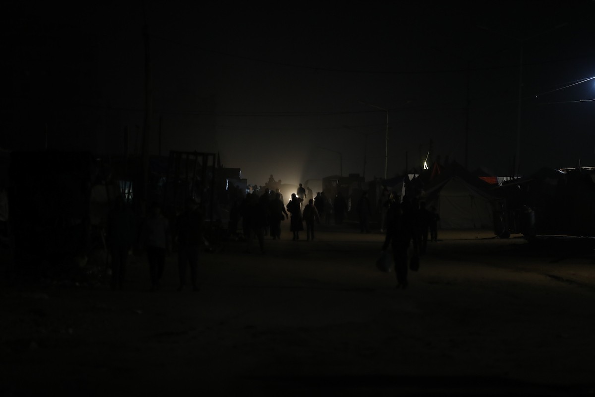 يسير فلسطينيون في أحد شوارع مدينة غزة، بينما يكافح النازحون في خيامهم لمواجهة الظلام، يتدفؤون ويطهون طعامهم بالحطب، محرومين حتى من أبسط مقومات الحياة، 23 يناير/كانون الثاني 2020. صورة: عمر أشتوي