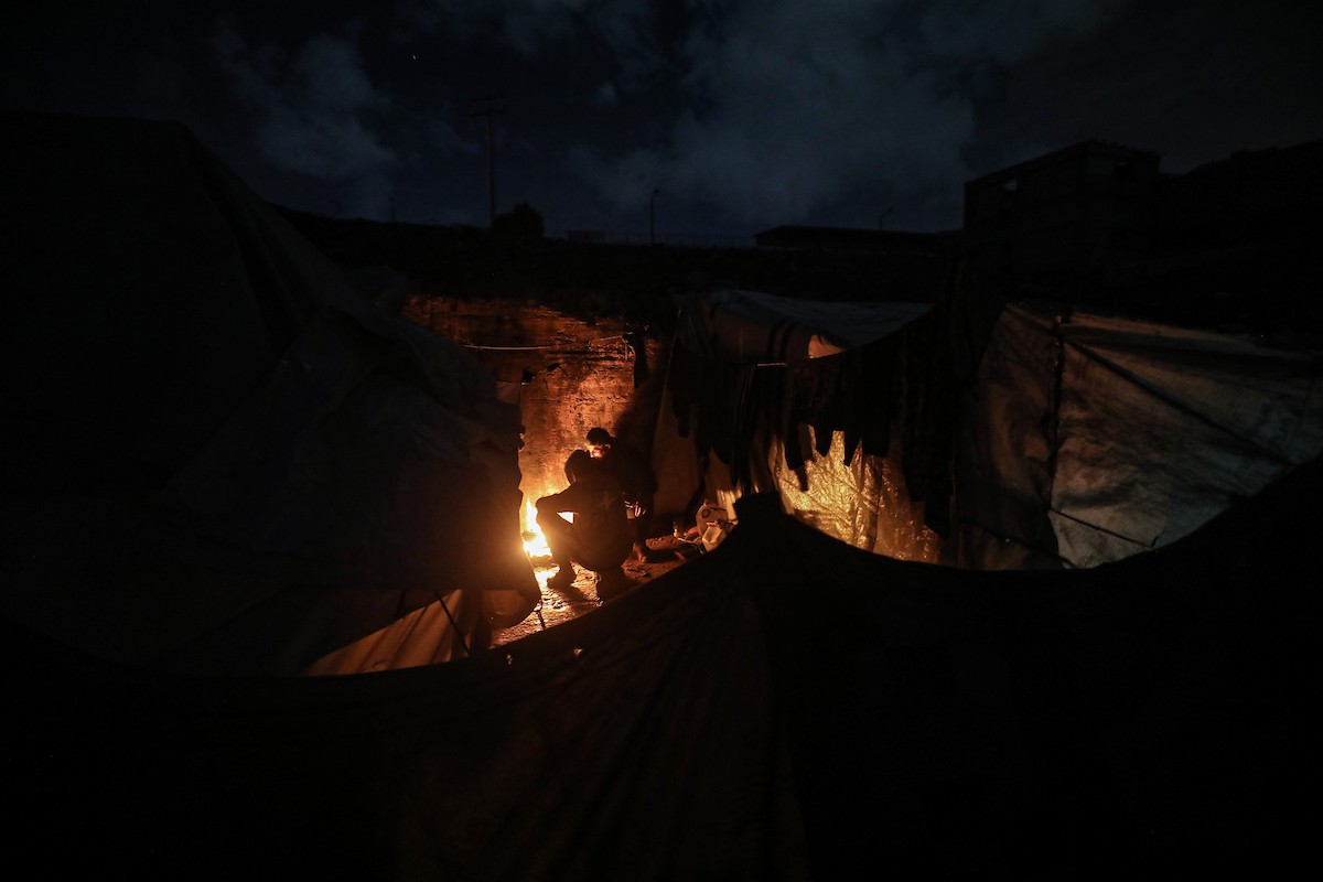 يسير فلسطينيون في أحد شوارع مدينة غزة، بينما يكافح النازحون في خيامهم لمواجهة الظلام، يتدفؤون ويطهون طعامهم بالحطب، محرومين حتى من أبسط مقومات الحياة، 19 يناير/كانون الثاني 2026. صورة: عمر أشتوي