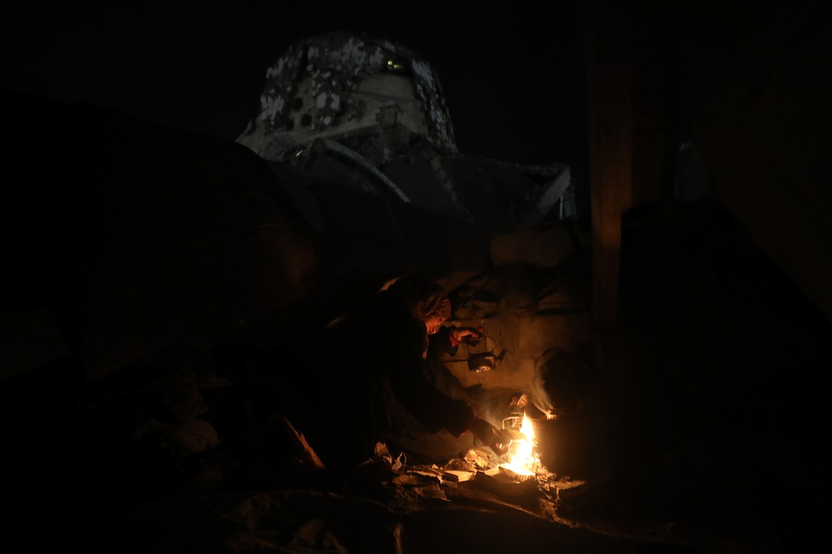 يسير فلسطينيون في أحد شوارع مدينة غزة، بينما يكافح النازحون في خيامهم لمواجهة الظلام، يتدفؤون ويطهون طعامهم بالحطب، محرومين حتى من أبسط مقومات الحياة، 23 يناير/كانون الثاني 2020. صورة: عمر أشتوي