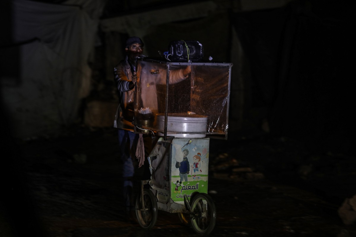 يسير فلسطينيون في أحد شوارع مدينة غزة، بينما يكافح النازحون في خيامهم لمواجهة الظلام، يتدفؤون ويطهون طعامهم بالحطب، محرومين حتى من أبسط مقومات الحياة، 19 يناير/كانون الثاني 2026. صورة: عمر أشتوي