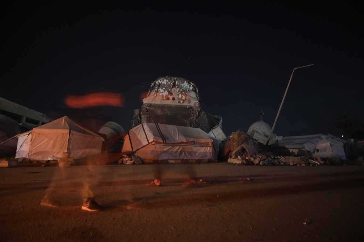 يسير فلسطينيون في أحد شوارع مدينة غزة، بينما يكافح النازحون في خيامهم لمواجهة الظلام، يتدفؤون ويطهون طعامهم بالحطب، محرومين حتى من أبسط مقومات الحياة، 23 يناير/كانون الثاني 2020. صورة: عمر أشتوي