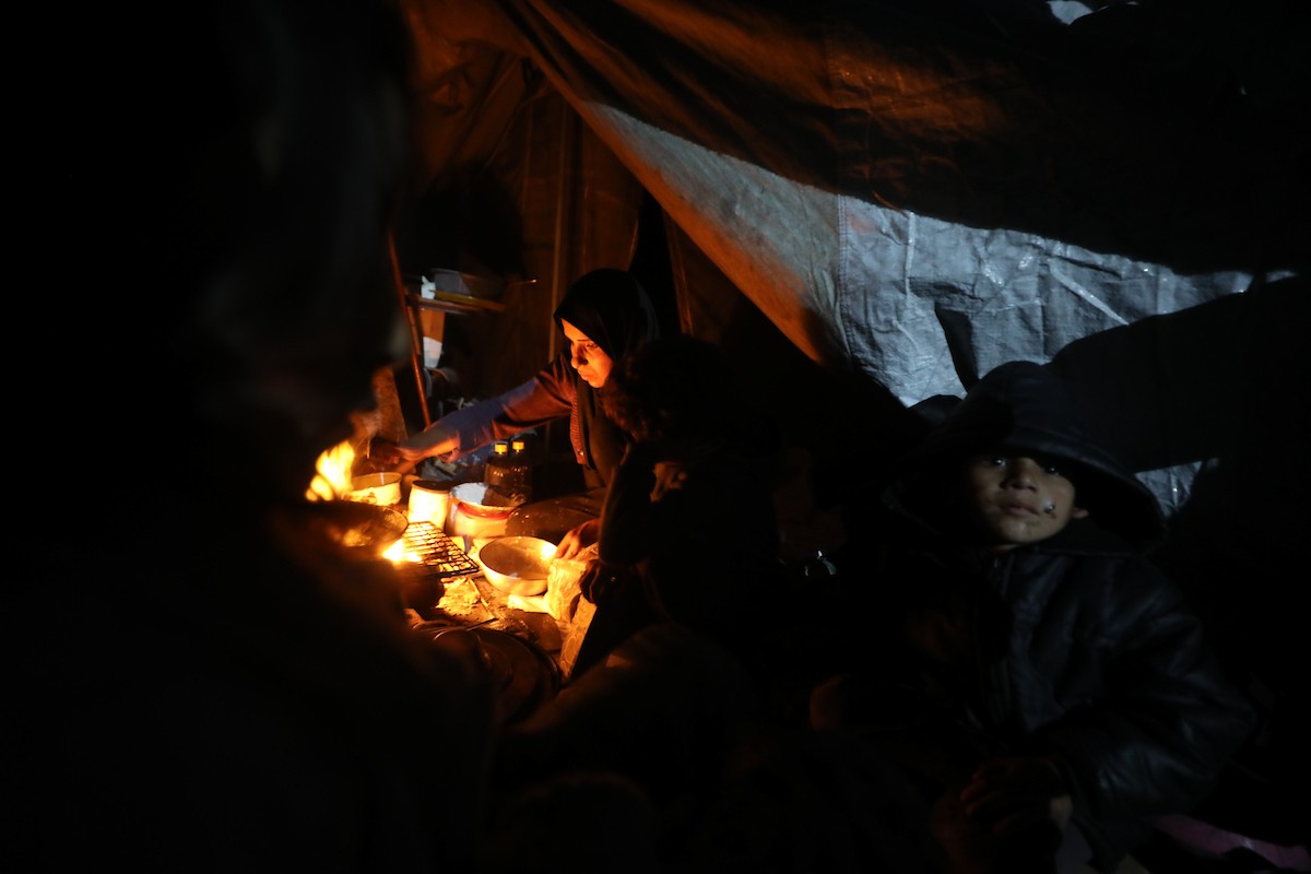 يسير فلسطينيون في أحد شوارع مدينة غزة، بينما يكافح النازحون في خيامهم لمواجهة الظلام، يتدفؤون ويطهون طعامهم بالحطب، محرومين حتى من أبسط مقومات الحياة، 23 يناير/كانون الثاني 2020. صورة: عمر أشتوي