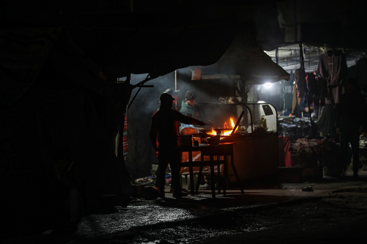 يسير فلسطينيون في أحد شوارع مدينة غزة، بينما يكافح النازحون في خيامهم لمواجهة الظلام، يتدفؤون ويطهون طعامهم بالحطب، محرومين حتى من أبسط مقومات الحياة، 19 يناير/كانون الثاني 2026. صورة: عمر أشتوي