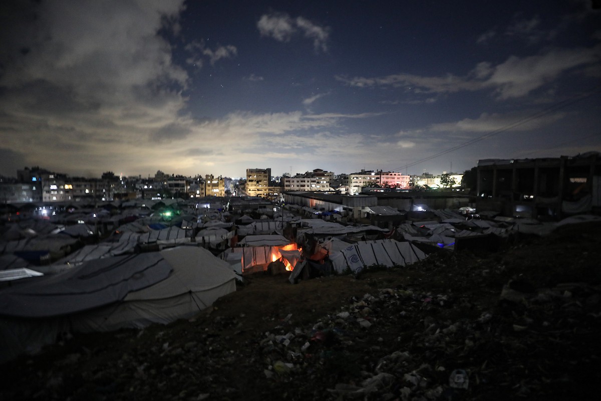 يسير فلسطينيون في أحد شوارع مدينة غزة، بينما يكافح النازحون في خيامهم لمواجهة الظلام، يتدفؤون ويطهون طعامهم بالحطب، محرومين حتى من أبسط مقومات الحياة، 19 يناير/كانون الثاني 2026. صورة: عمر أشتوي