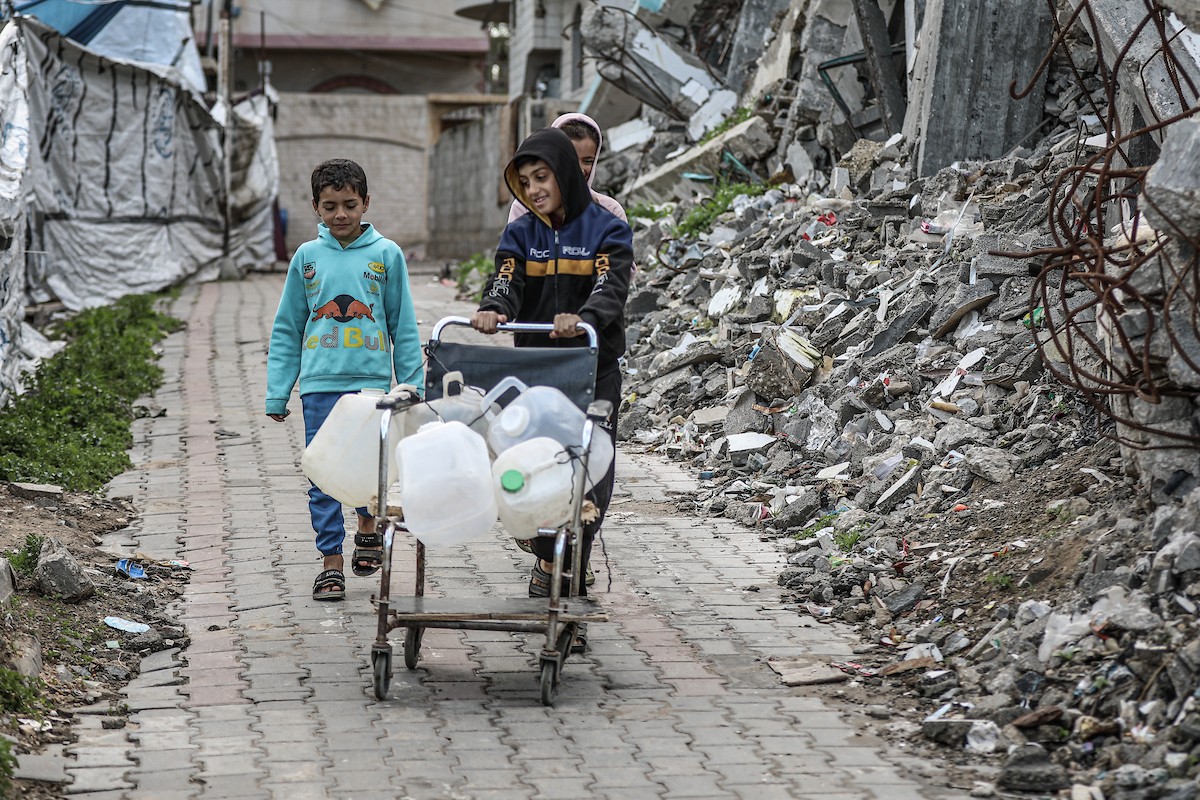 يملأ الفلسطينيون جالوناتهم بالمياه التي توزعها صهاريج المياه، وينقلونها إلى خيامهم في مخيم النصيرات، حيث تفاقمت أزمة المياه نتيجة الأضرار الجسيمة التي لحقت بالبنية التحتية جراء الهجمات الإسرائيلية. النصيرات، وسط قطاع غزة، 29 يناير/كانون الثاني 2026. صورة: رمزي أبو عامر