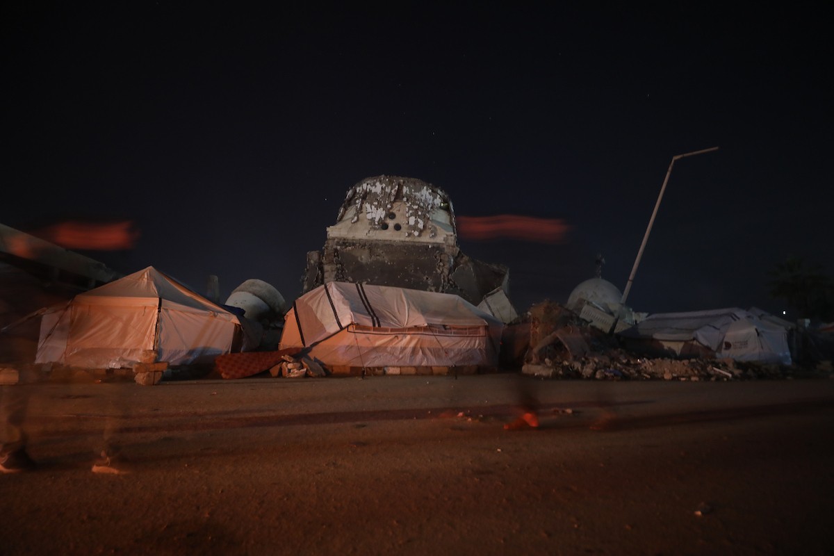 يسير فلسطينيون في أحد شوارع مدينة غزة، بينما يكافح النازحون في خيامهم لمواجهة الظلام، يتدفؤون ويطهون طعامهم بالحطب، محرومين حتى من أبسط مقومات الحياة، 23 يناير/كانون الثاني 2020. صورة: عمر أشتوي