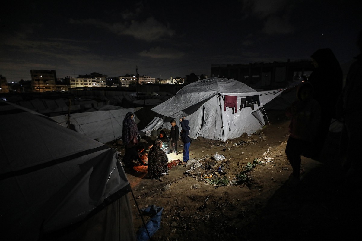 يسير فلسطينيون في أحد شوارع مدينة غزة، بينما يكافح النازحون في خيامهم لمواجهة الظلام، يتدفؤون ويطهون طعامهم بالحطب، محرومين حتى من أبسط مقومات الحياة، 19 يناير/كانون الثاني 2026. صورة: عمر أشتوي